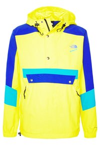 Giacca leggera e colorata con corpo giallo brillante, dettagli blu e turchese, cappuccio, chiusura frontale con bottoni automatici e polsini elasticizzati.