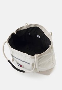 Canvas tote bag i off-white med svart inredning. Har rund dragsko-stängning, en zip-ficka och en logotypetikett på framsidan.