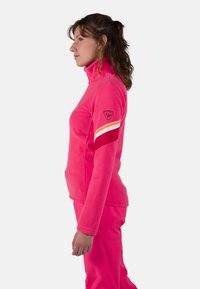 Roze fleece pullover met een hoge kraag, met een sportief ontwerp. Accenten van verticale strepen in oranje, wit en rood op de mouw.