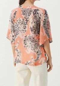 Blouse légère à manches courtes en pêche avec un motif paisley noir et blanc. Coupe ample, encolure ronde et tissu doux et texturé.