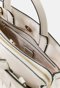 Sac à main crème en cuir avec surface texturée, ferrures dorées, poche intérieure zippée et bordure noire. L'intérieur comporte une étiquette logo.