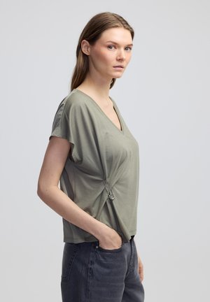 Olivově zelený top s véčkovým výstřihem vyrobený z měkké látky, s krátkými rukávy a nařaseným detailem, s kovovým prvkem ve stříbrné barvě po straně.