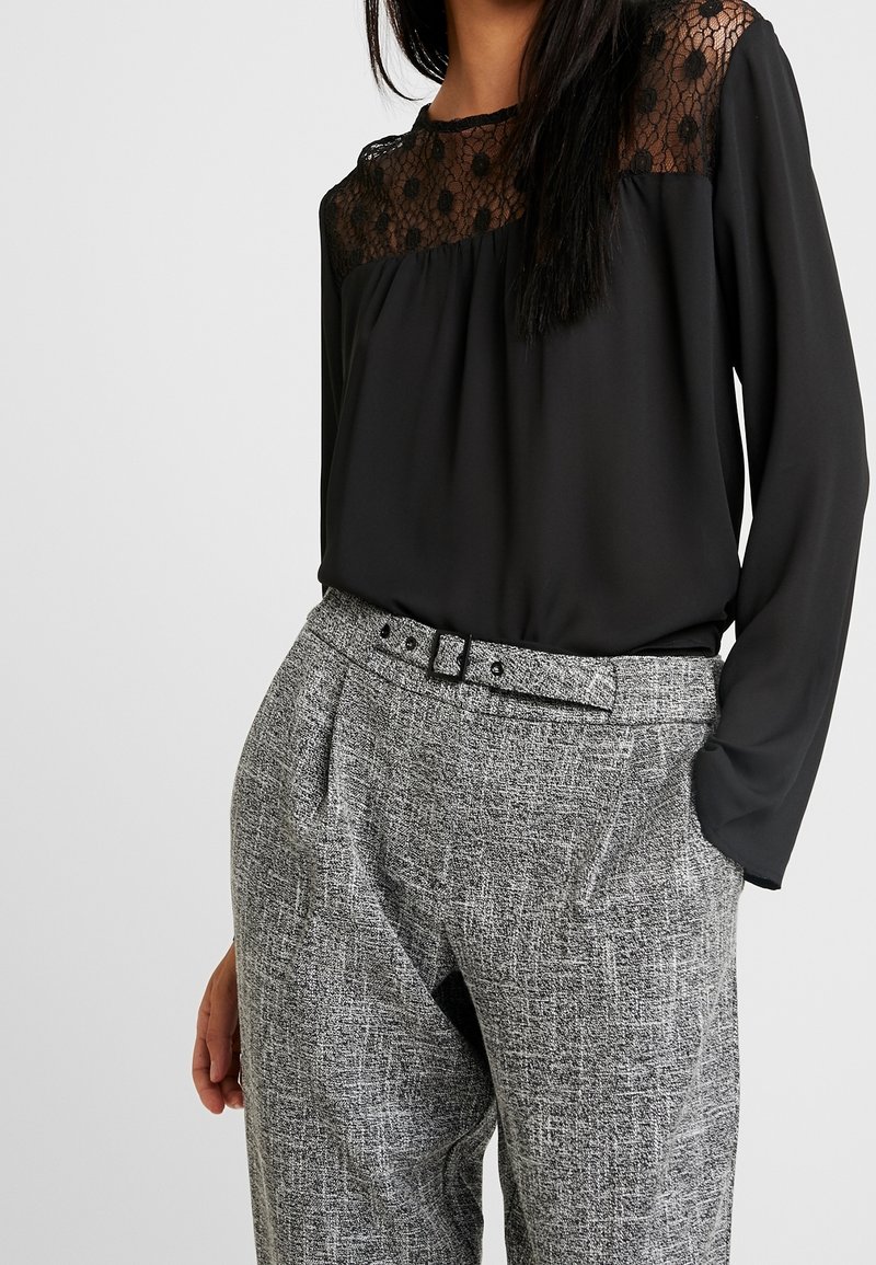 Czarna bluzka z koronkowym karczkiem z okrągłymi wzorami, połączona z teksturowanymi szarymi spodniami w kratę i cienkim czarnym paskiem.