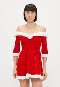 Rdeča žametna obleka z off-the-shoulder dizajnom, belim umetnim krznom na rokavih in robu ter razširjenim krilom.