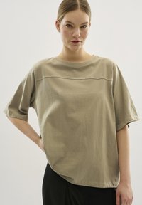 Camiseta de manga corta oversize beige, hecha de algodón suave, con un escote redondeado y una costura horizontal en el pecho.