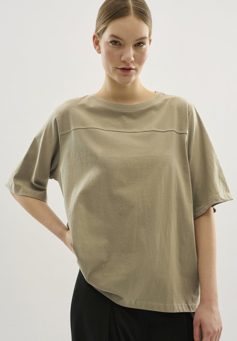 Beżowy, oversize t-shirt z krótkim rękawem, wykonany z miękkiej bawełny, z okrągłym dekoltem i poziomą szwem na wysokości klatki piersiowej.
