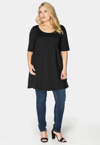 Sort tunika med rund halsudskæring og korte ærmer, parret med mørkeblå stramme jeans. Stoffet ser blødt ud og hænger løst.