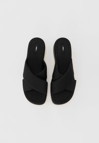 Mustad mustad sandaalid, millel on ristuvat kangast rihmad, lame tald ja tikitud detailid tekstureeritud sisetaldbel. Brändi logo on nähtav sisetaldil.