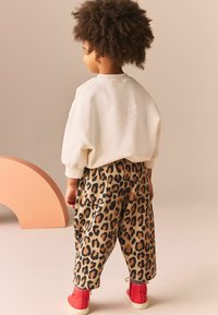 Pull crème et pantalon à imprimé léopard beige avec des taches marron foncé. Chaussures montantes rouges. Tissu doux avec une coupe ample.