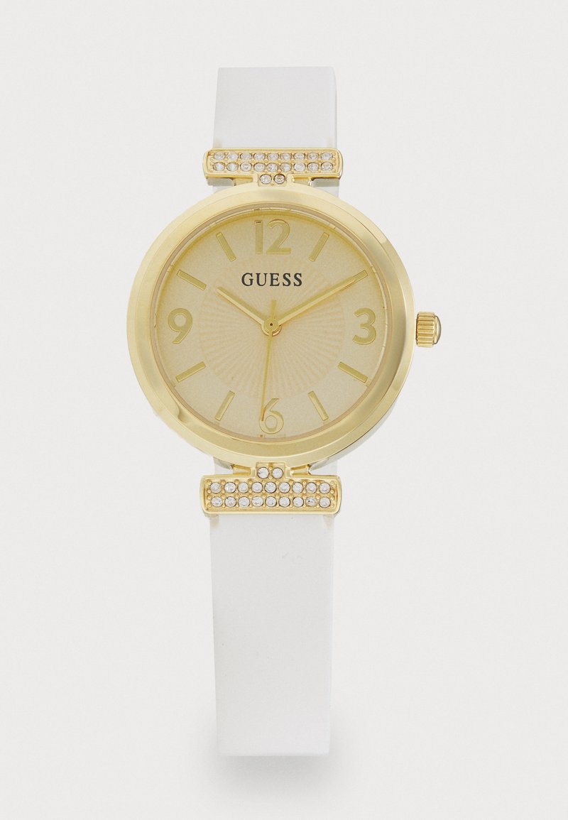 Gold-tone analog watch with a white silicone strap. Features a textured gold dial, clear accents on the bezel, and crystal embellishments.
