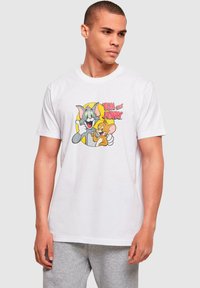 Camiseta de algodón blanca con un estampado colorido de los personajes de dibujos animados Tom y Jerry, con contornos negros gruesos y acentos amarillos.