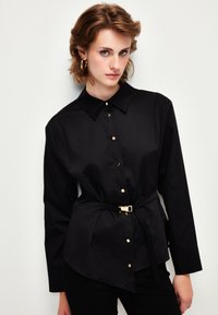 Camicia nera con bottoni in tessuto liscio, con colletto, maniche lunghe, bottoni dorati e una cintura con fibbia dorata.