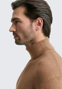 Brauner Rollkragenpullover aus weichem Material, mit einem gerippten Kragen und subtiler Textur. Das Modell ist im Profil vor einem neutralen Hintergrund zu sehen.