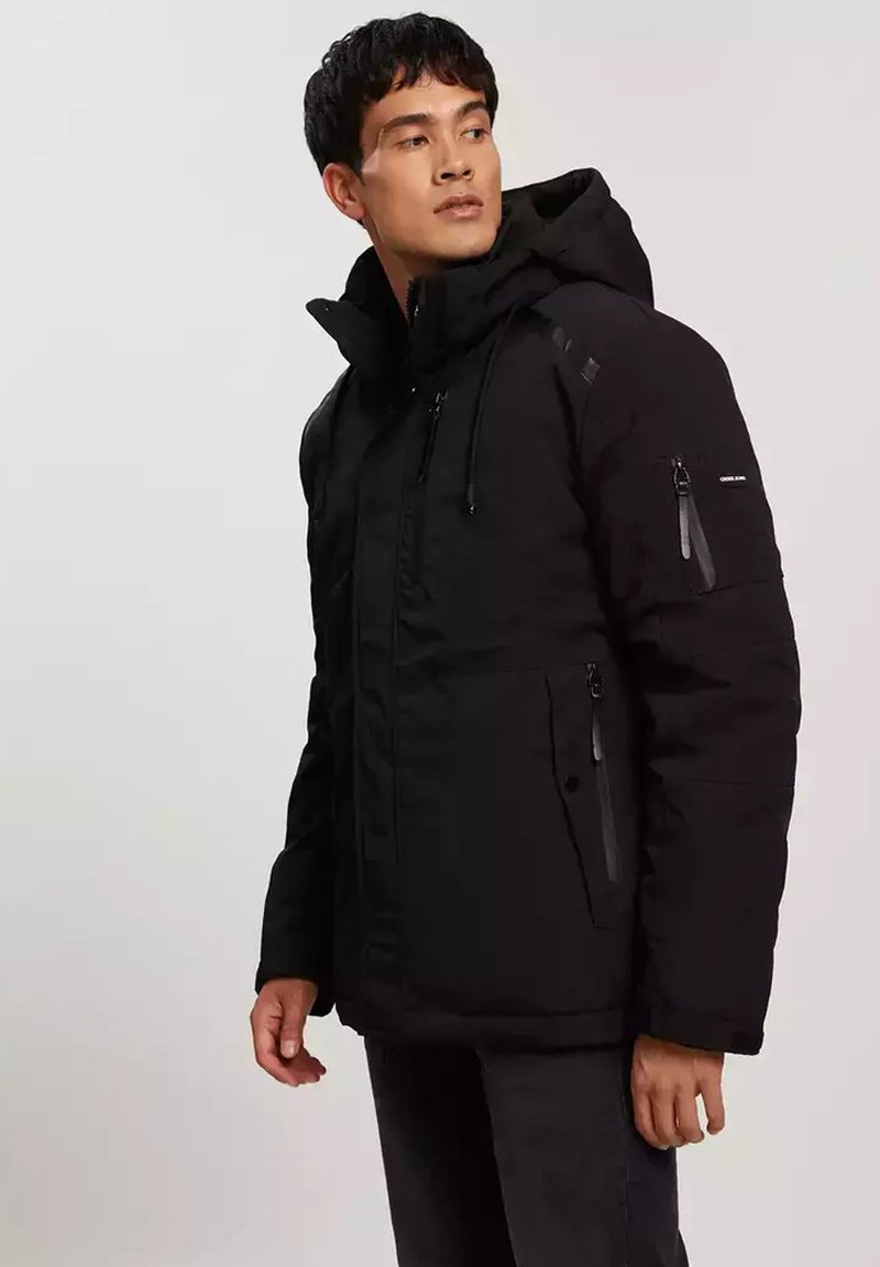 Czarna ocieplana kurtka z kapturem, zapinanymi na zamek kieszeniami, regulowanymi sznurkami i wyściółką zapewniającą ciepło. Teksturowana tkanina z akcentami.