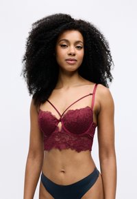 Burgundin pitsilä bralette, jossa on nauhakuvio, kukkakuosiset yksityiskohdat ja aaltonen helma, yhdistettynä tummansävyisiin bikinihousuihin.