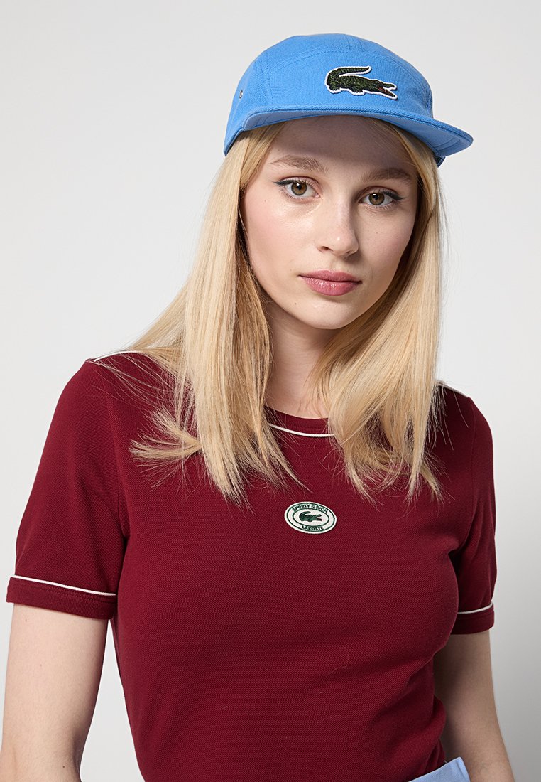 Blauwe pet met een platte klep en geborduurd groen krokodil logo, gecombineerd met een bordeauxrood shirt met een rond logo en witte bies.