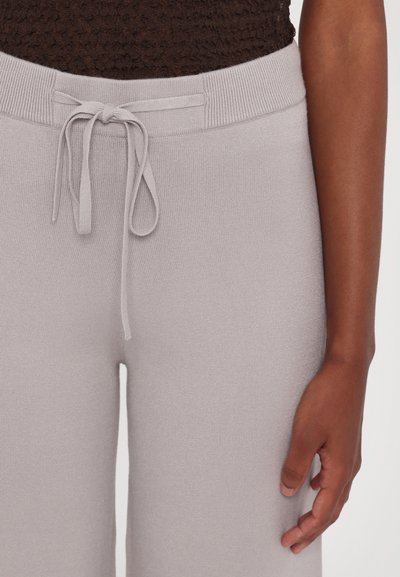 Light gray knit joggers with a drawstring waistband, featuring a soft texture and a relaxed fit, displayed alongside a hand.