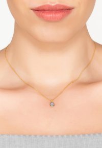 Goldkette mit einem tropfenförmigen, facettierten Stein in Hellblau, eingefasst in einem schmalen goldenen Rahmen. Glatte Textur, zartes Design.