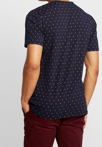 Marineblå kortærmet t-shirt med prikker i lys rosa. Stof virker blødt med en afslappet pasform. Bagfra ses rund halsudskæring.