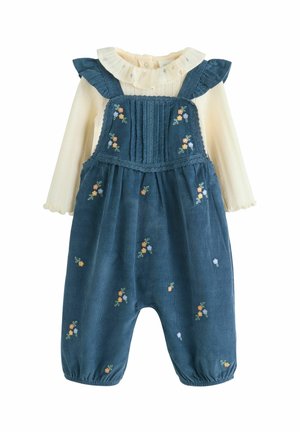Blaue Corduroy-Latzhosen mit floralem Stickmuster, Rüschen-Schulterträgern und einem weißen, strukturierten Langarmhemd darunter.