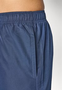 Tengerészkék sport rövidnadrág elasztikus derékkal, texturált anyaggal és oldalsó zsebekkel, sima felülettel.