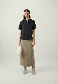 Sort kortærmet skjorte med knapkrave, parret med en lang beige denimnederdel og grå ankelstøvler. Inkluderer en hvid håndtaske.