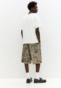 Hvid oversized t-shirt med korte ærmer, parret med khaki shorts med et naturinspireret print, sorte sko og hvide sokker.