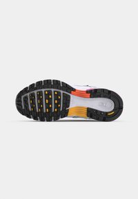Suela de zapatilla deportiva en negro y gris con dibujo multidireccional, destacando acentos en naranja y amarillo y una superficie texturizada para mejorar el agarre.