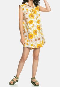 El vestido sin mangas con estampado floral presenta un diseño de botones, con girasoles amarillos predominantes sobre un fondo claro y un corte relajado.