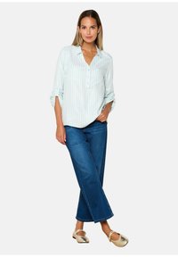 Blusa a righe in azzurro chiaro con bottoni frontali, maniche arrotolate, abbinata a jeans larghi blu scuro e ballerine metallizzate dorate.