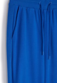 Niebieskie dresy z prążkowanym pasem w talii i sznurkiem do regulacji, z bocznymi kieszeniami i gładką fakturą materiału.