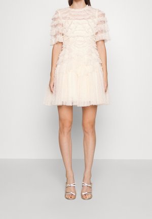 Robe courte crème avec manches et corsage transparents à volants. Jupe en tulle superposée avec texture à pois et plis subtils. Sandales argentées.