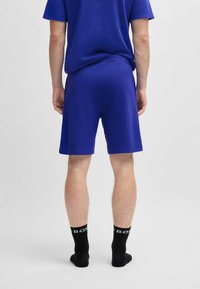 Blauwe sportshorts van een gestructureerde stof, met een ontspannen pasvorm en een zoom die tot halverwege de dij komt, gedragen met zwarte kousen tot de crew met een logo.