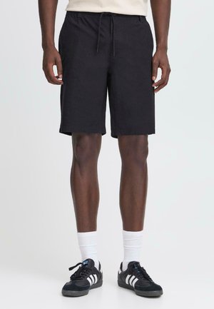 Pantalones cortos de algodón negro con cintura elástica y cordón. Corte a la altura de la rodilla; combinados con zapatillas negras y calcetines blancos.