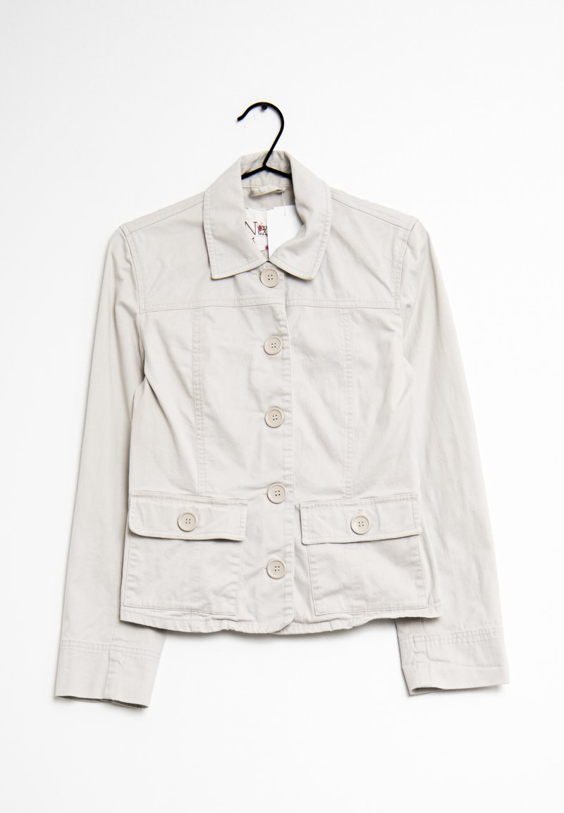 Veste beige clair à boutons avec col et deux poches rabats à l'avant, suspendue sur un cintre noir sur fond blanc.