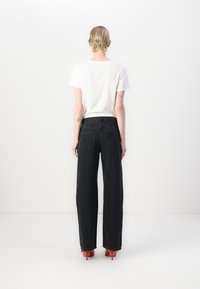 Black wide-leg jeans with a high waist, featuring back pockets, paired with a plain white t-shirt and red high-heeled shoes.
