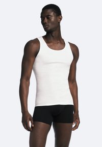 Hvid ribbet tanktop med rund halsudskæring, parret med sorte tætsiddende shorts, der viser en glat tekstur og en kropsnær pasform.