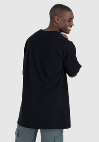 T-shirt nera oversize in cotone, con maniche corte e scollatura rotonda, mostrata da dietro con una texture liscia.