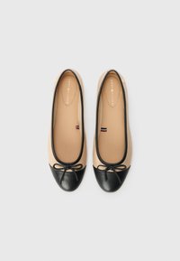 Paire de ballerines beige avec bouts noirs et petits nœuds, vues de dessus sur un fond clair.