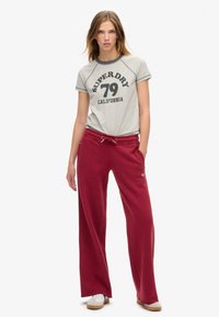 Camiseta gris con estampado negro "Superdry 79 California" combinada con pantalones de chándal holgados de color burdeos que cuentan con una cinturilla elástica y bolsillos.