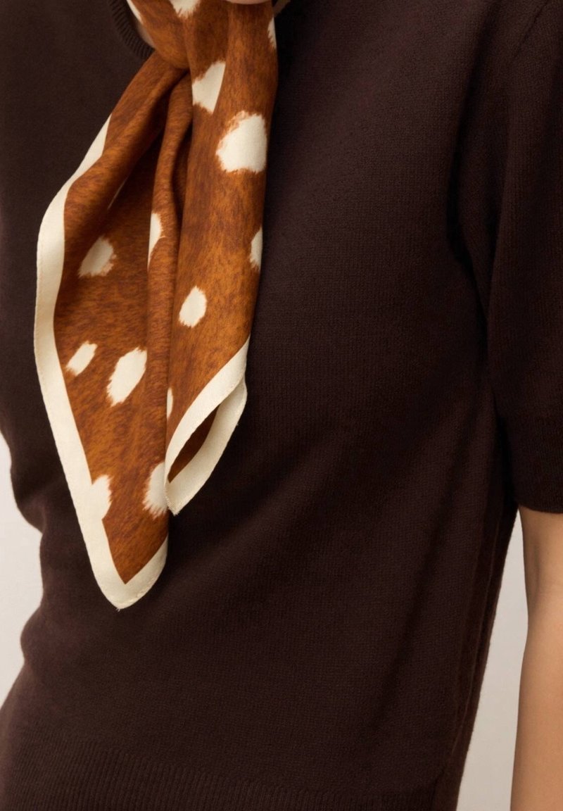Foulard à pois marron et blanc noué autour du cou sur un haut à manches courtes marron foncé.