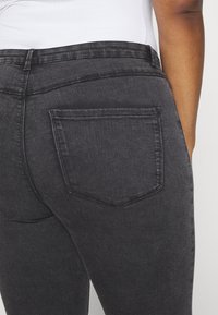 Vaqueros de mezclilla negros con una textura suave, que cuentan con un bolsillo trasero y una cinturilla de altura media. La tela presenta un brillo sutil.