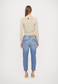 Jersey beige con relieve combinado con vaqueros azul claro. Los vaqueros tienen dos bolsillos traseros con diseños en forma de triángulo y un parche de cuero marrón; zapatos sin cordones.