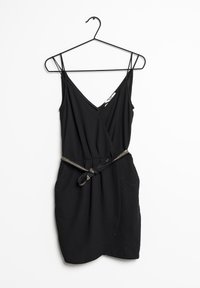 Vestido negro sin mangas con escote en V, diseño envolvente y un cinturón de tela a juego con un acento metálico. Textura suave. Cuelga de un gancho negro.