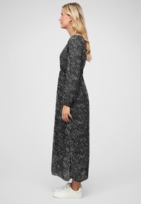 Black long-sleeve dress with white wave pattern, flowy fabric, cinched waist, and ankle-length, paired with white sneakers.