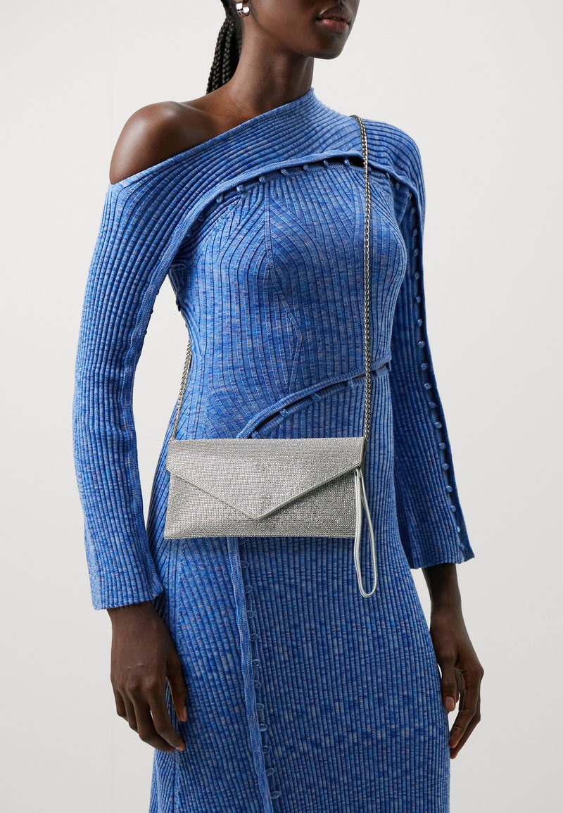 Silver mesh clutch bag with an envelope shape, worn crossbody. The textured blue ridged dress features an off-shoulder design and button accents.