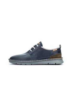 Zapato casual de cuero azul marino con cordones blancos, acento en tacón de ante marrón y suela de goma gris, vista lateral sobre fondo blanco.