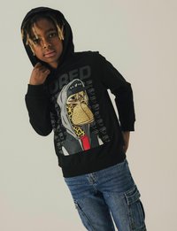 Zwarte hoodie met een cartoonontwerp van een karakter met een luipaardprint, vergezeld van het woord "BORED" in vette tekst.