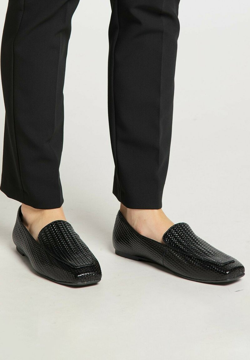 Zwarte loafers van gestructureerd leer, met een gevlochten patroon, vierkante neus en een platte zool, gecombineerd met zwarte op maat gemaakte broek.