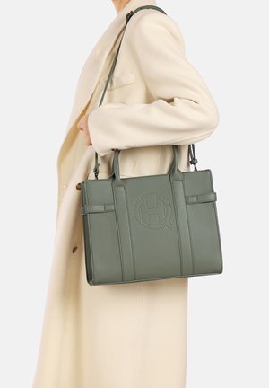 Borsa a mano verde in pelle con finitura testurizzata, forma strutturata, doppi manici e logo impresso sulla parte anteriore. Accompagnata da un cappotto crema.